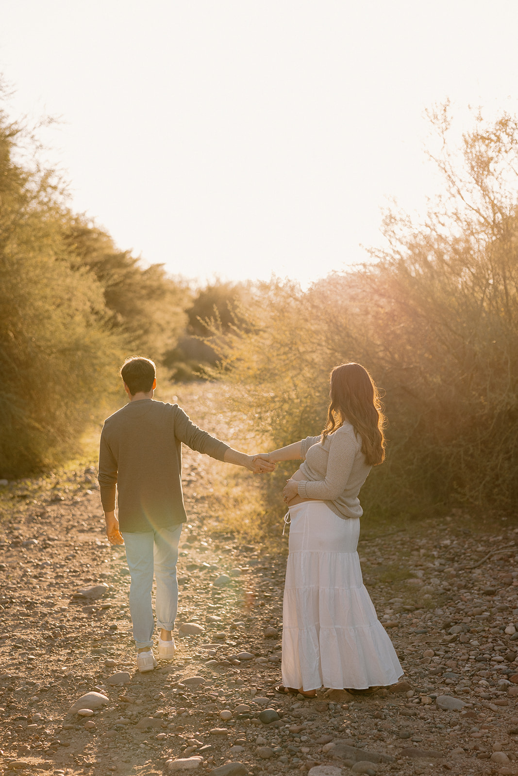 Pregnant couple walking hand in hand along a desert trail at golden hour in Phoenix
