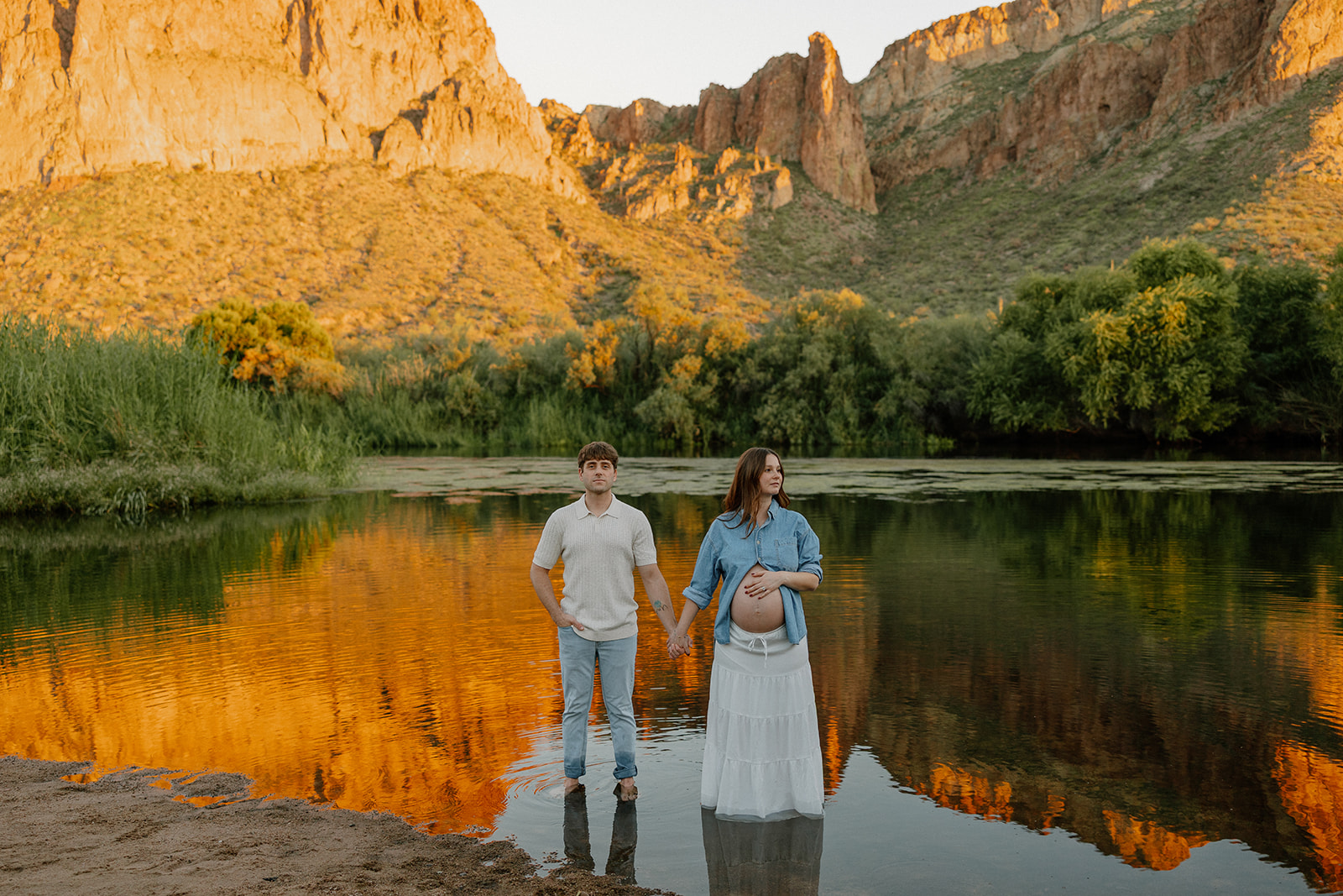 Couple standing in the Salt River holding hands with golden mountain reflections behind them