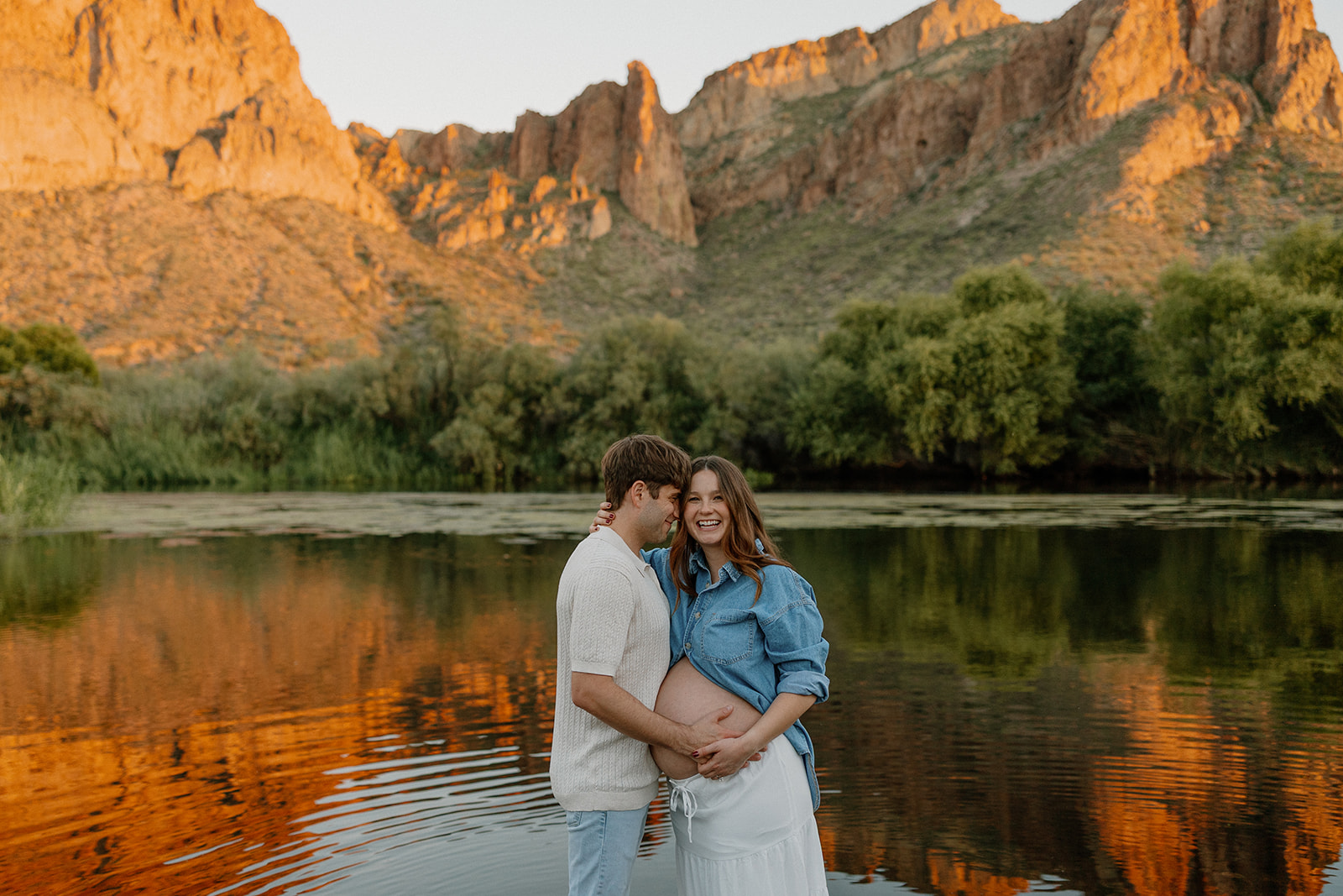 Couple embracing in the Salt River at sunset with mountains reflecting in the water, Arizona maternity photographer
