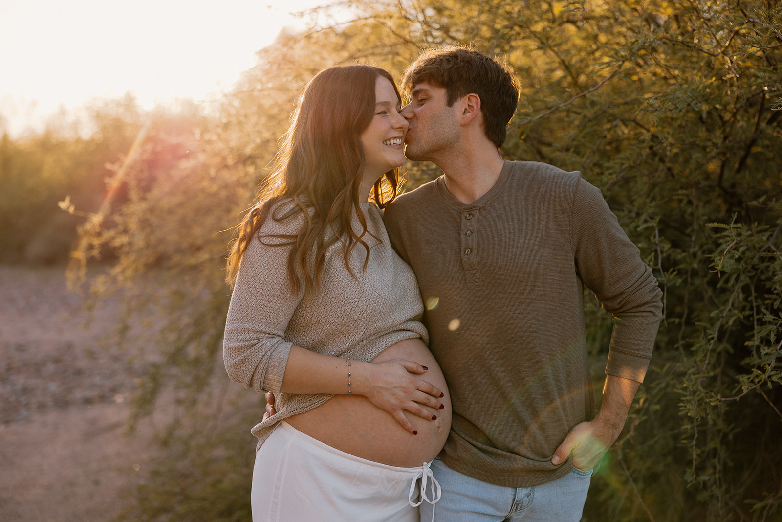 Couple smiling together on a desert path during golden hour maternity session
