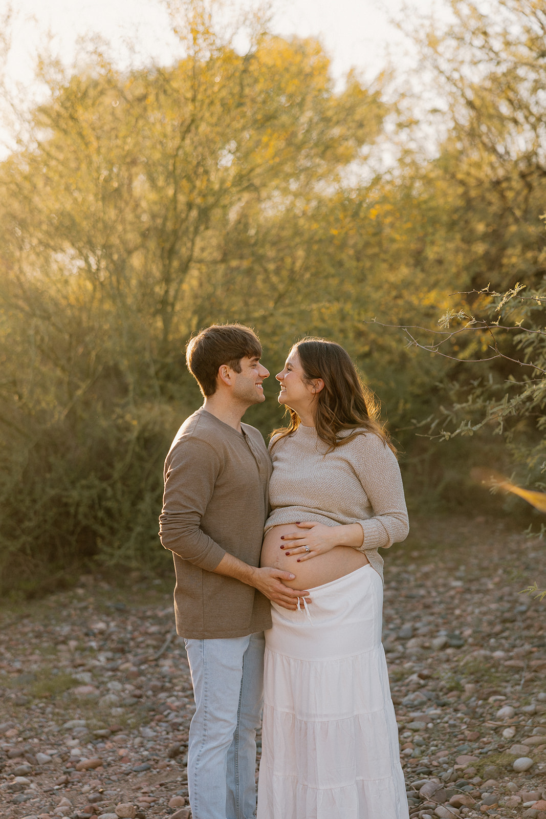 Expecting couple smiling together on a quiet desert path during sunset maternity photos in Arizona
