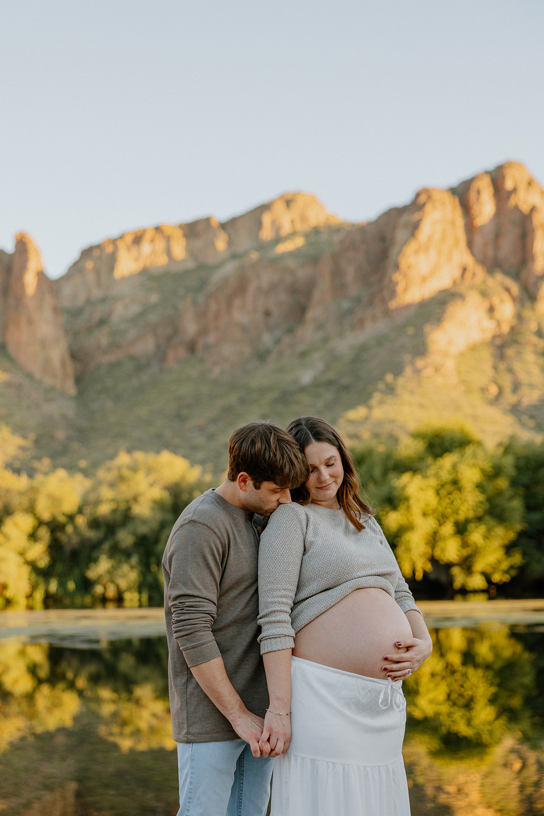 Couple standing close together in the river at sunset with warm reflections and mountain backdrop, Arizona maternity photographer