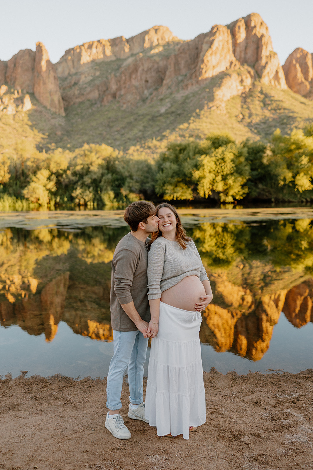 Couple laughing together by the water with mountains in the background, Arizona maternity photographer
