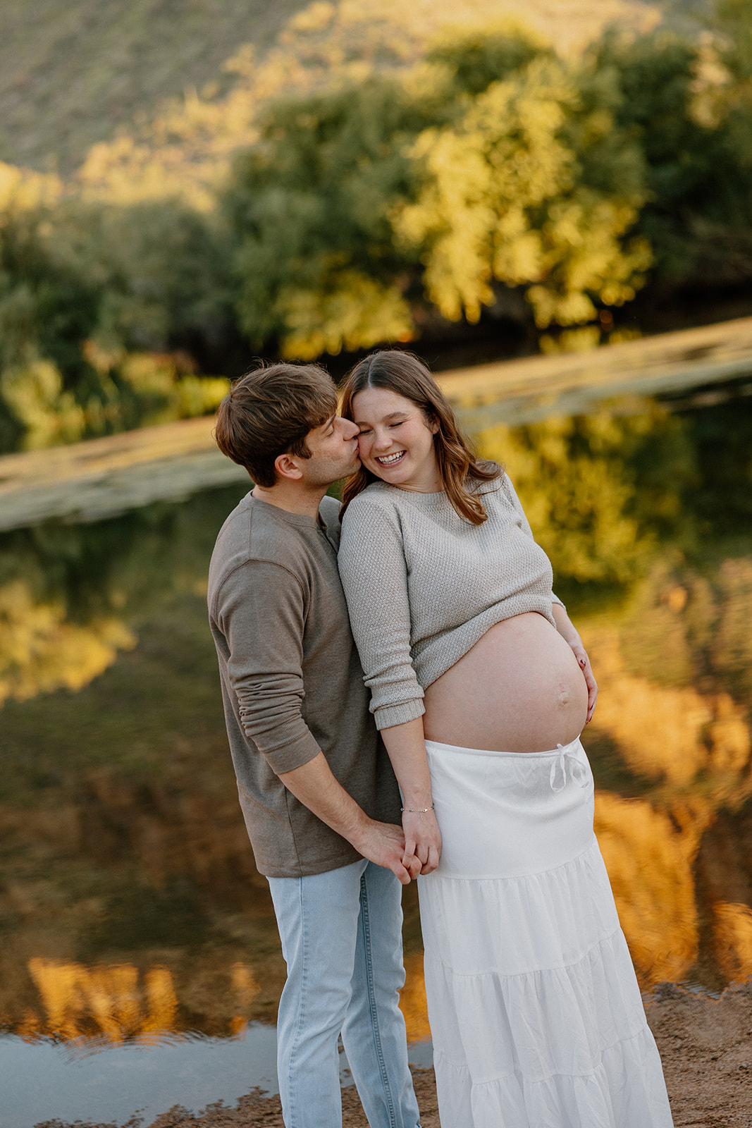 Couple embracing by the water with warm reflections and soft evening tones
