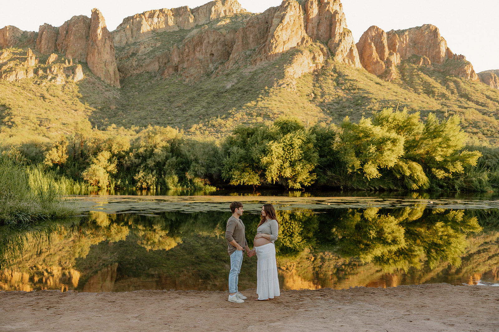Wide landscape maternity photo of couple standing by the river with mountains mirrored in the water, Arizona maternity photographer

