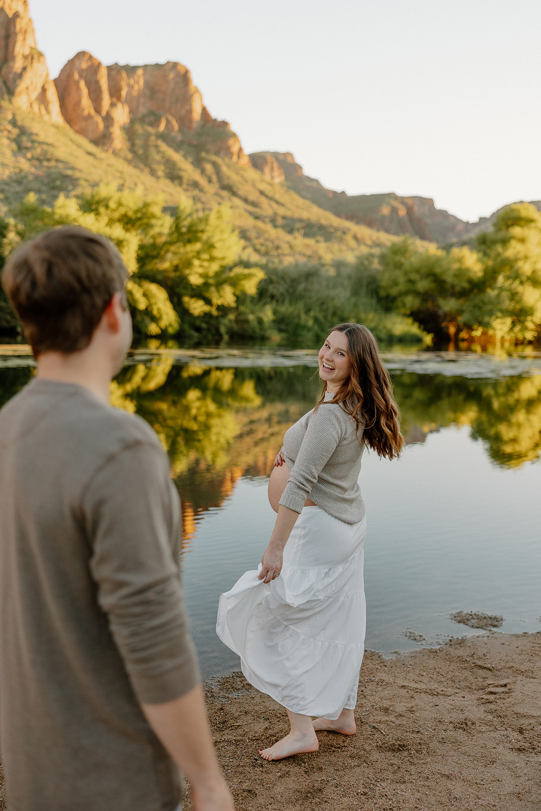 Pregnant woman walking barefoot along the riverbank while partner watches, Arizona maternity photographer