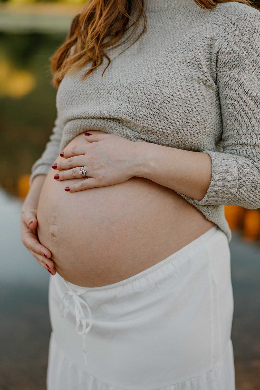 Close-up detail of baby bump with hands resting gently on stomach in natural light
