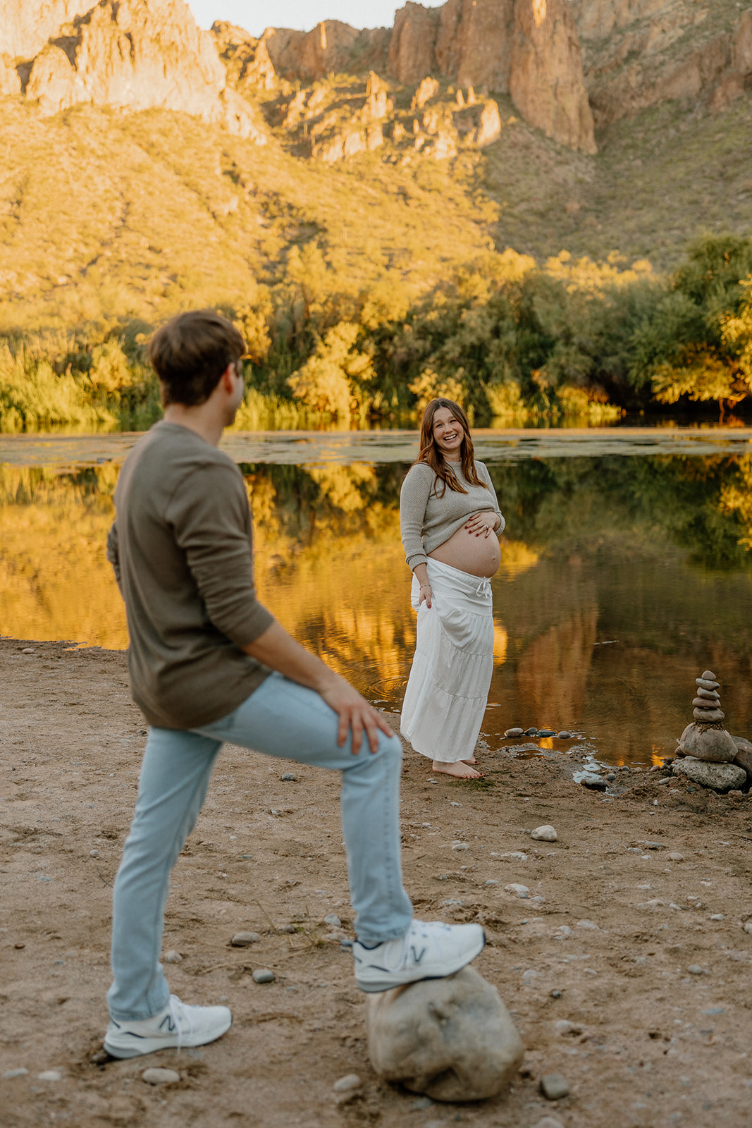 Playful maternity moment with couple near the river and desert mountains in the background, Arizona maternity photographer
