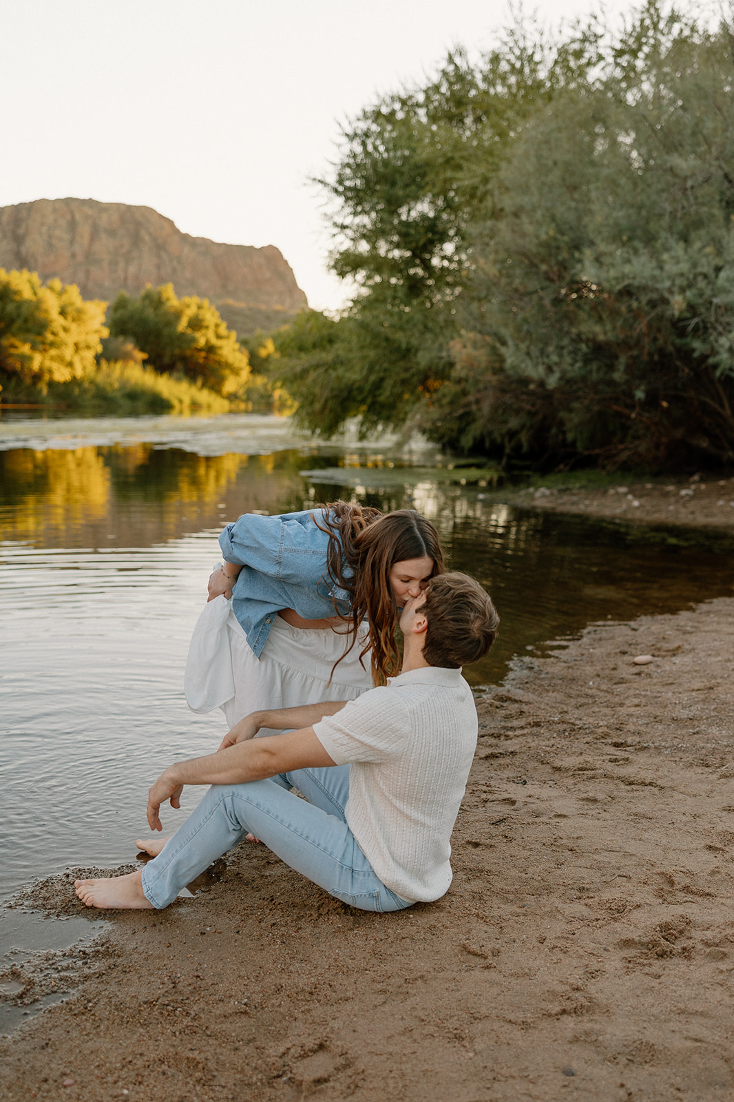 Couple kissing while sitting on the riverbank during a relaxed maternity session, Arizona maternity photographer
