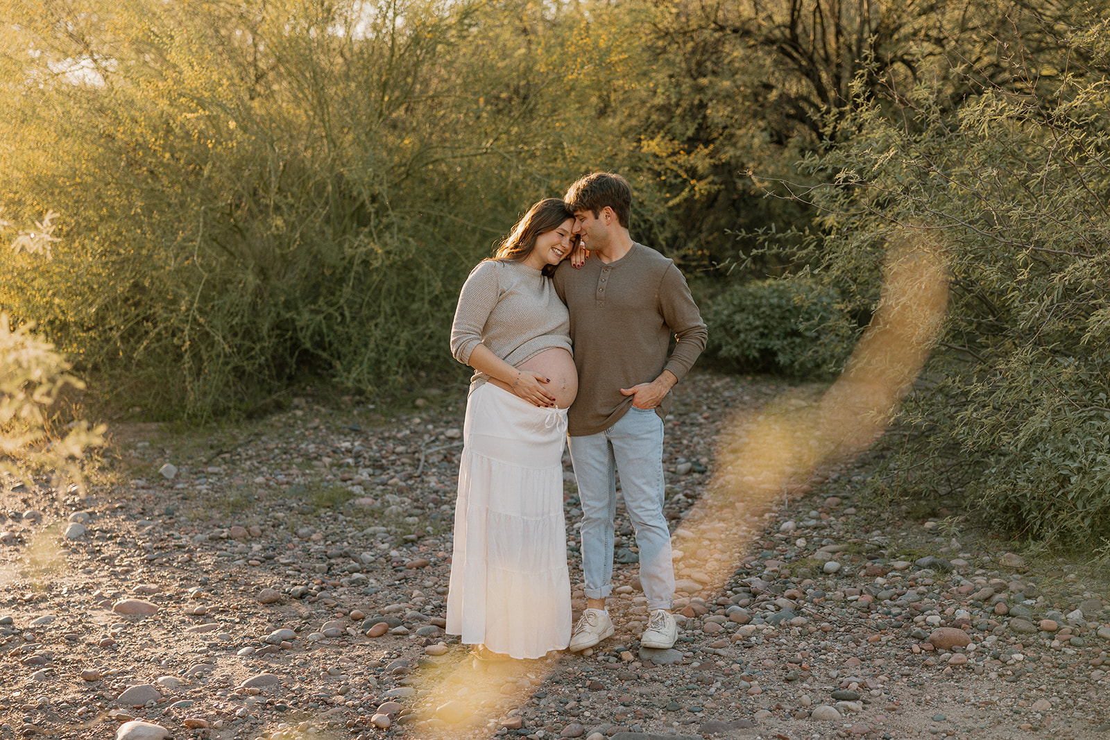 Expecting couple standing together on a desert trail surrounded by warm golden light

