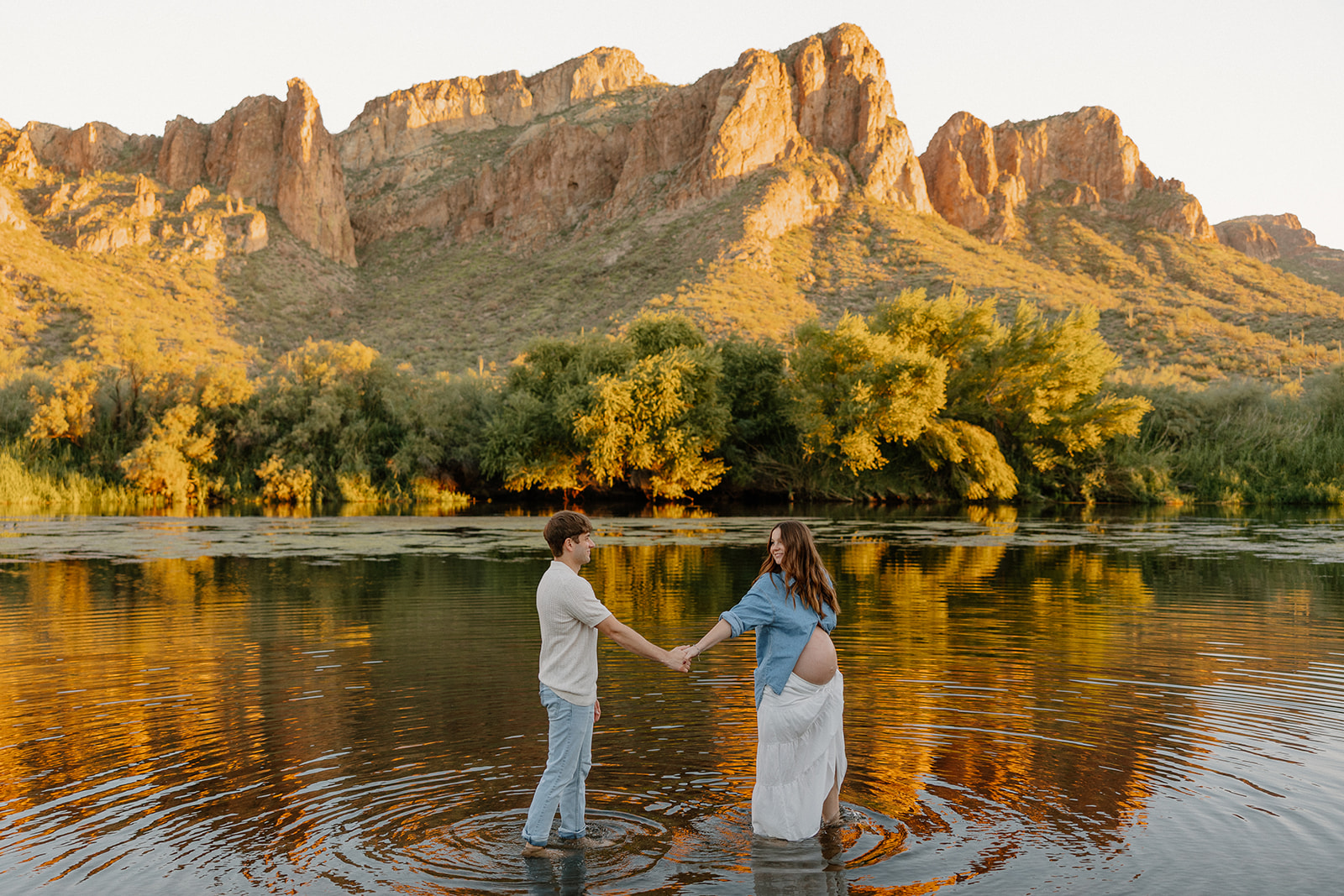 Couple holding hands in the water with wide mountain views and golden reflections in Arizona
