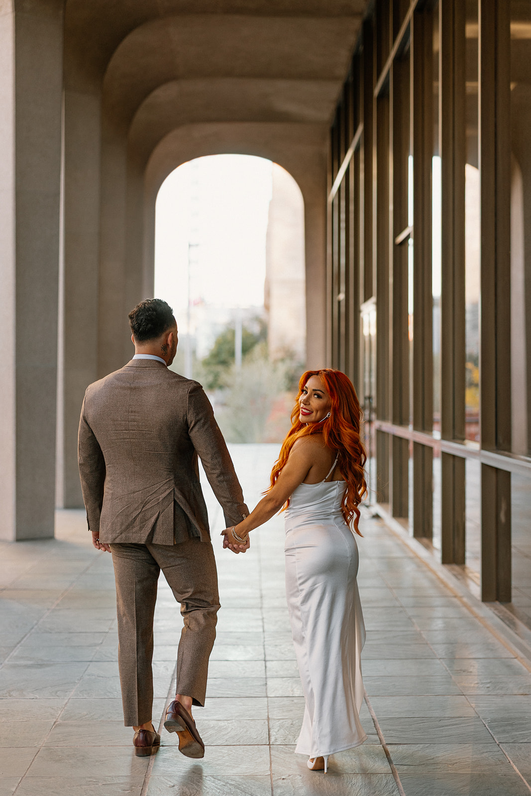 Couple walking hand in hand under modern archways in downtown Phoenix engagement session

