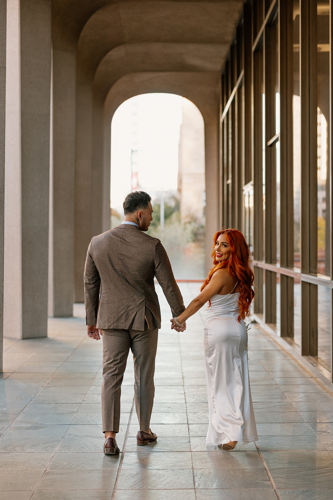 Couple walking hand in hand under modern downtown arches during phoenix engagement photos
