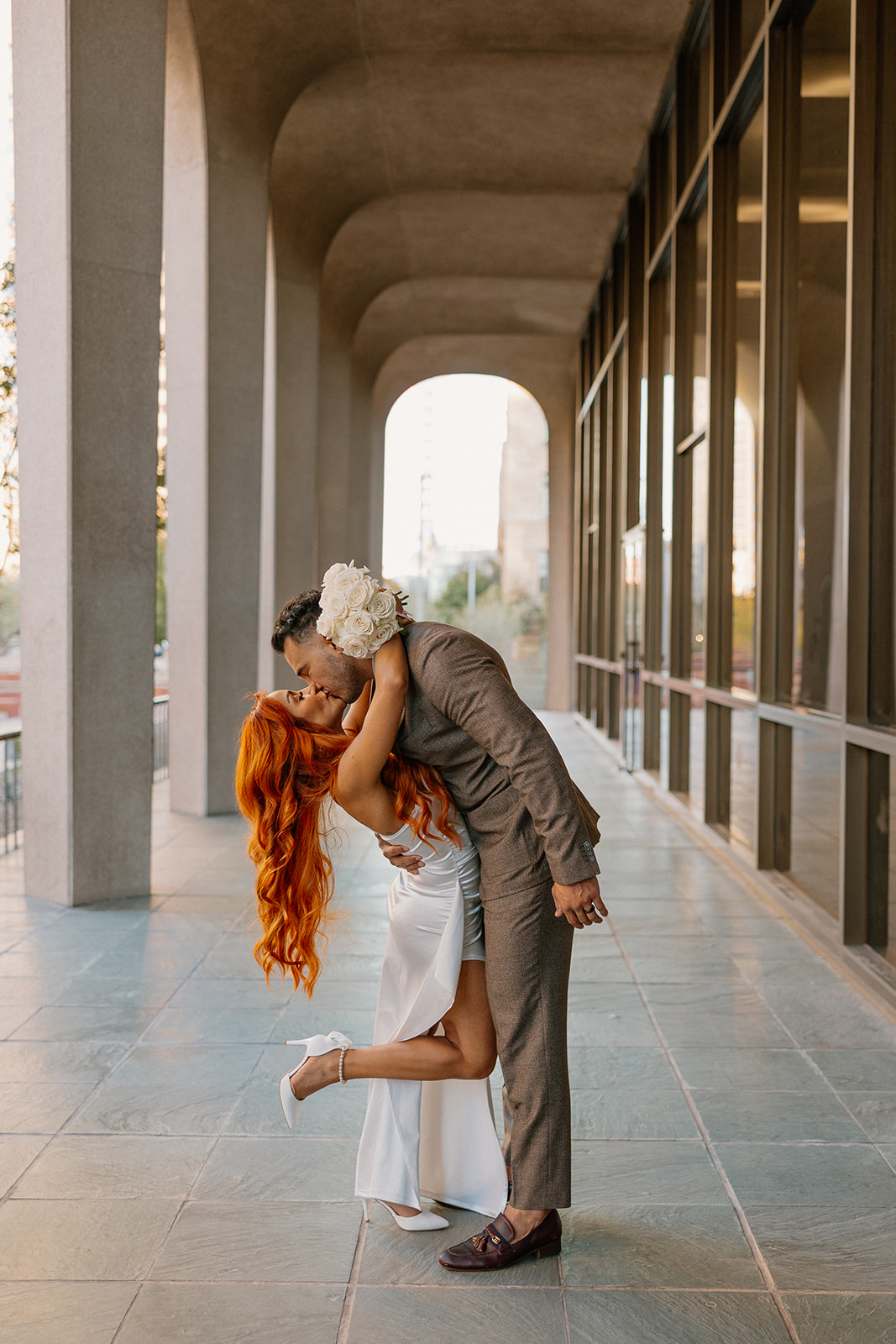 Couple kissing under modern architectural arches during downtown engagement session
