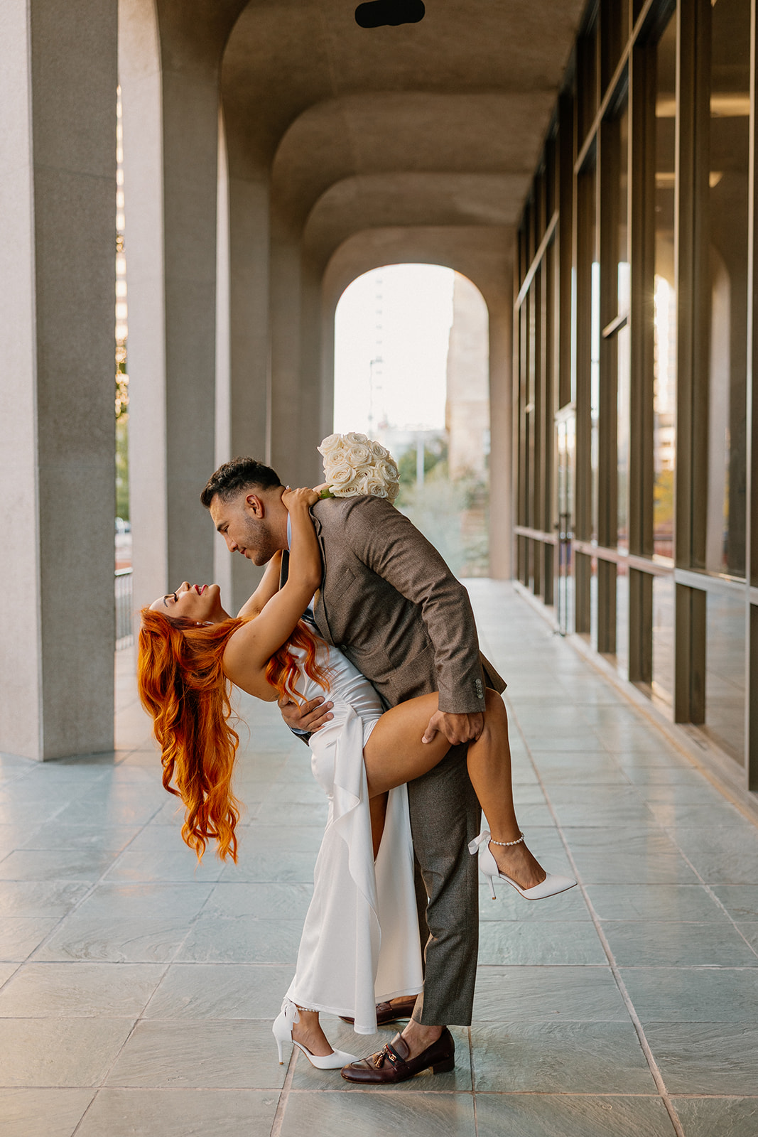 Groom dipping bride for a romantic kiss under modern architectural arches during phoenix engagement photos
