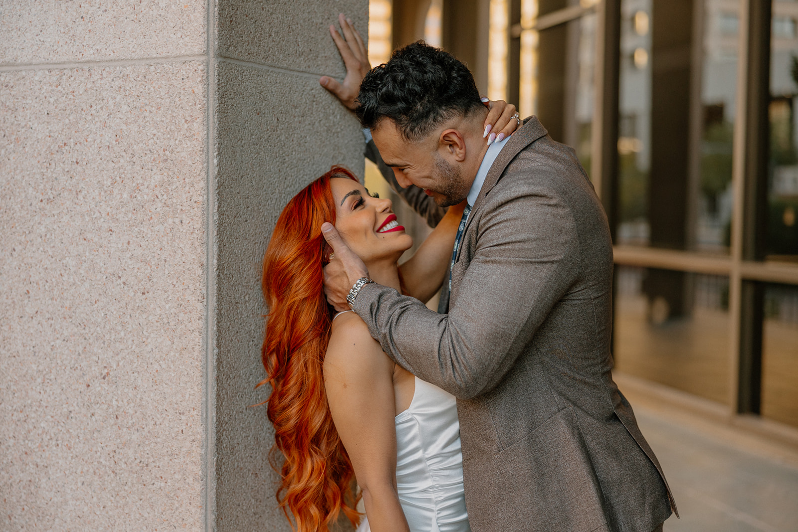Couple laughing together beside modern building columns during downtown phoenix engagement photos
