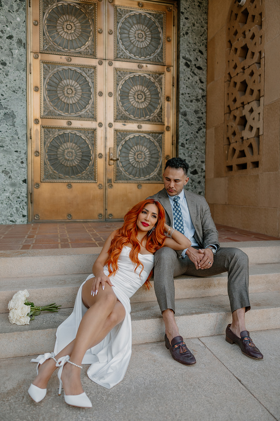 Couple sitting together on city hall steps in front of ornate gold doors in downtown Phoenix
