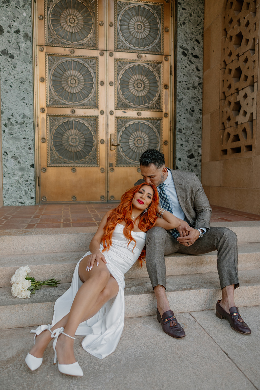 Couple cuddling on steps in front of decorative gold doors during engagement session
