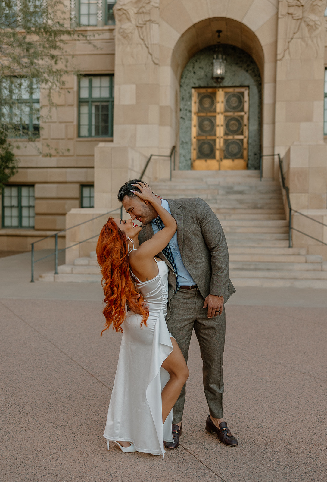Couple embracing and kissing in front of historic building entrance in downtown Phoenix

