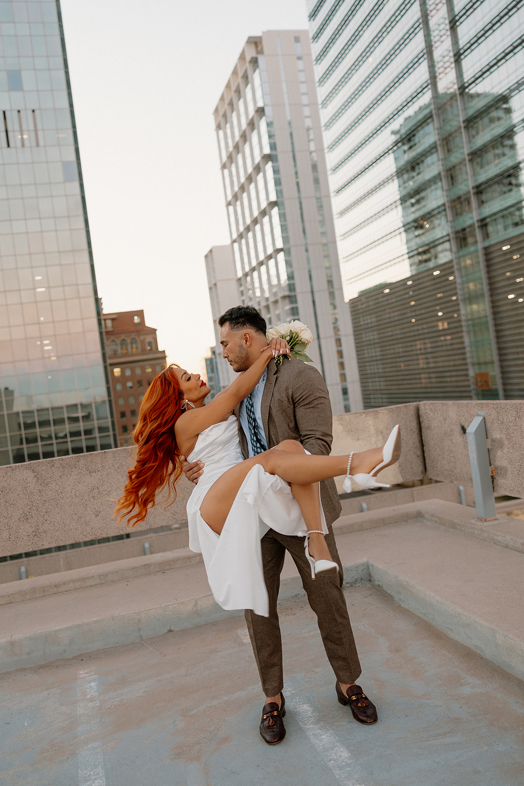 Groom lifting bride on rooftop with city skyline during phoenix engagement photos
