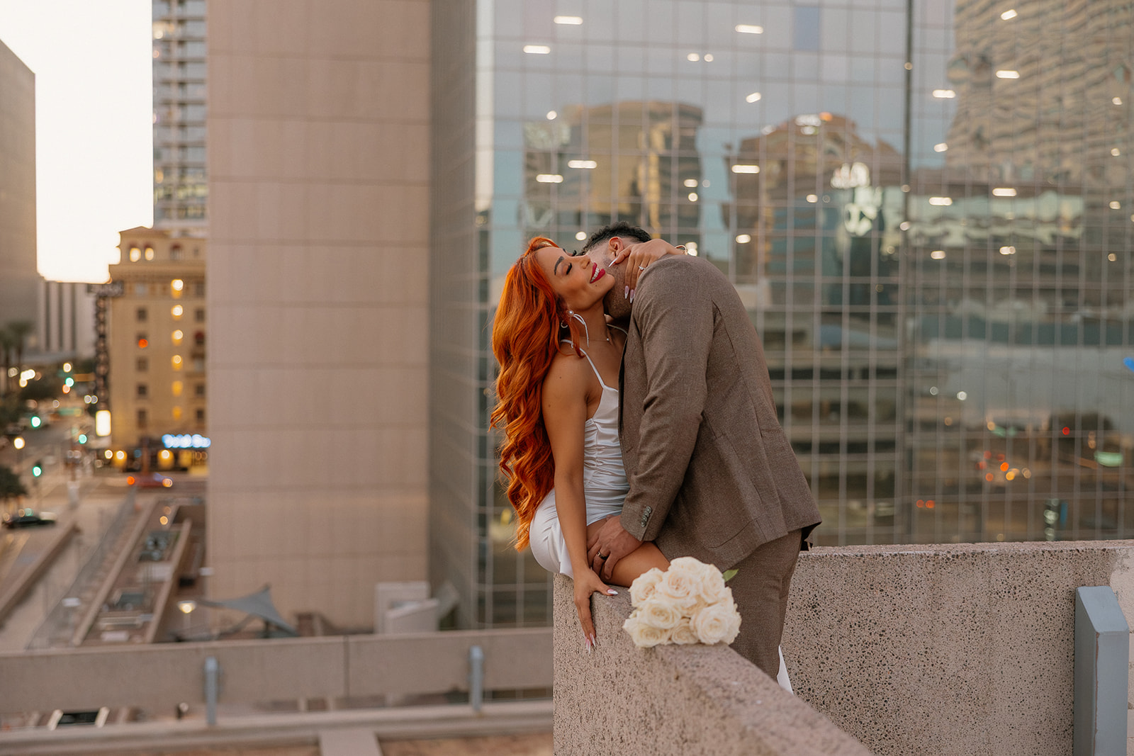 Romantic rooftop moment of couple embracing with city skyline at sunset in downtown Phoenix engagement session
