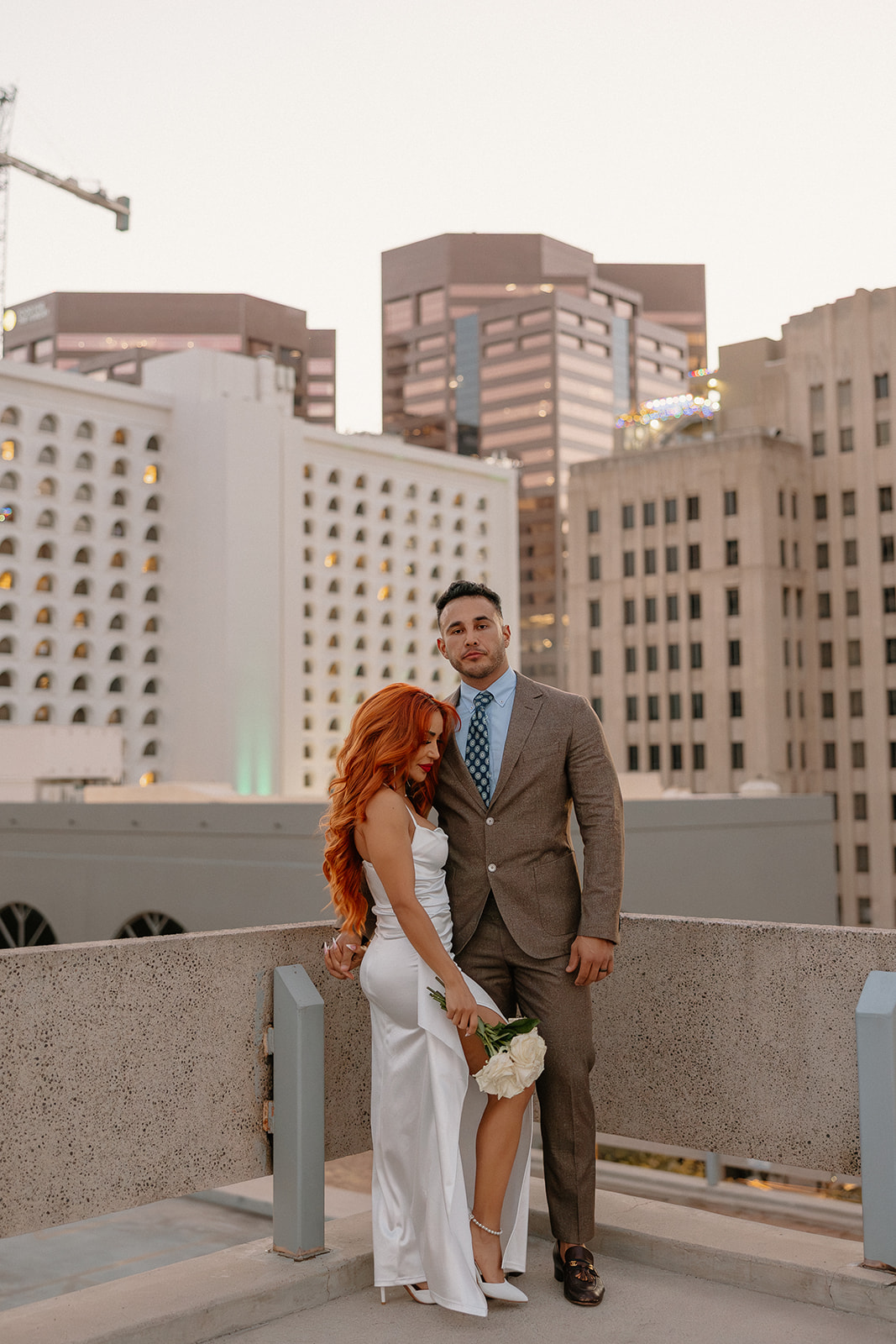 Couple posing together on rooftop with downtown skyline during phoenix engagement photos
