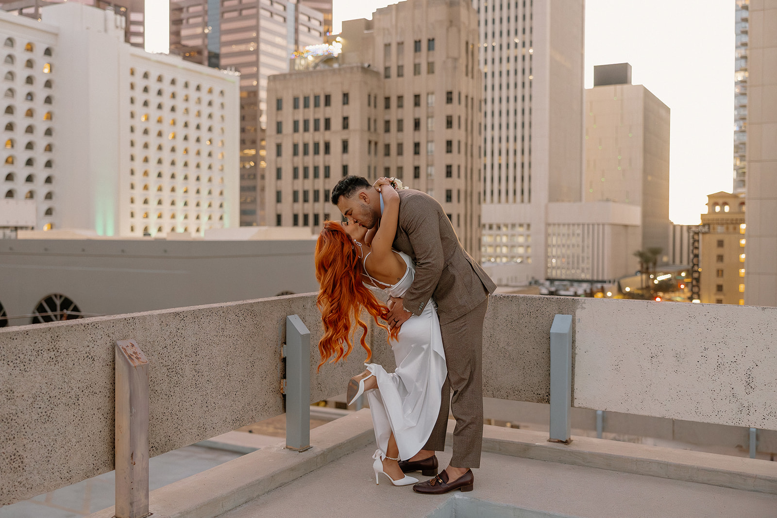 Couple kissing on rooftop at sunset with downtown skyline during phoenix engagement photos
