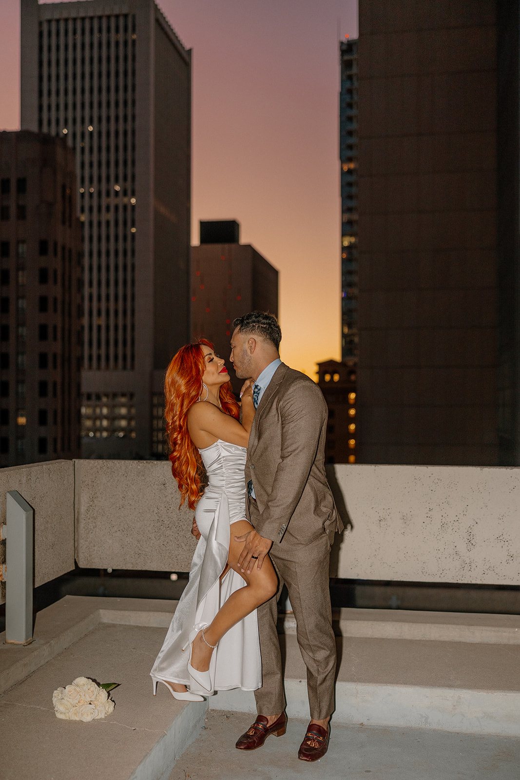 Couple embracing on rooftop at sunset with glowing downtown skyline during phoenix engagement photos
