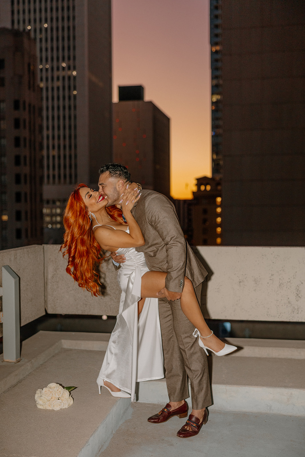 Groom lifting bride playfully on rooftop at sunset during phoenix engagement photos
