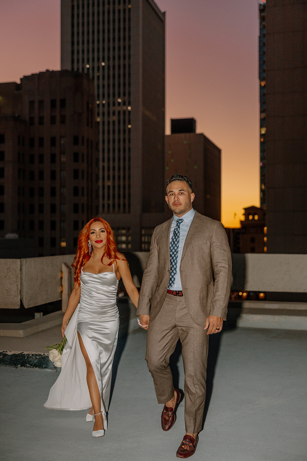 Couple holding hands and walking across rooftop at sunset during phoenix engagement photos

