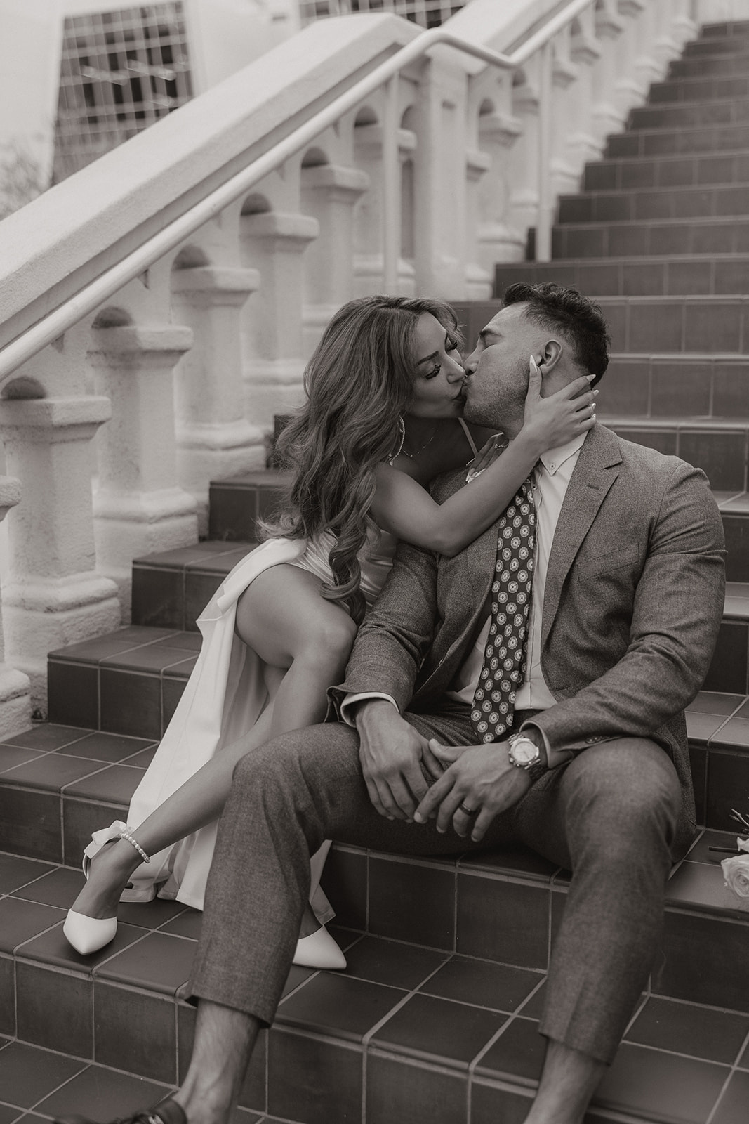 Black and white photo of couple kissing while sitting on tiled staircase in downtown Phoenix

