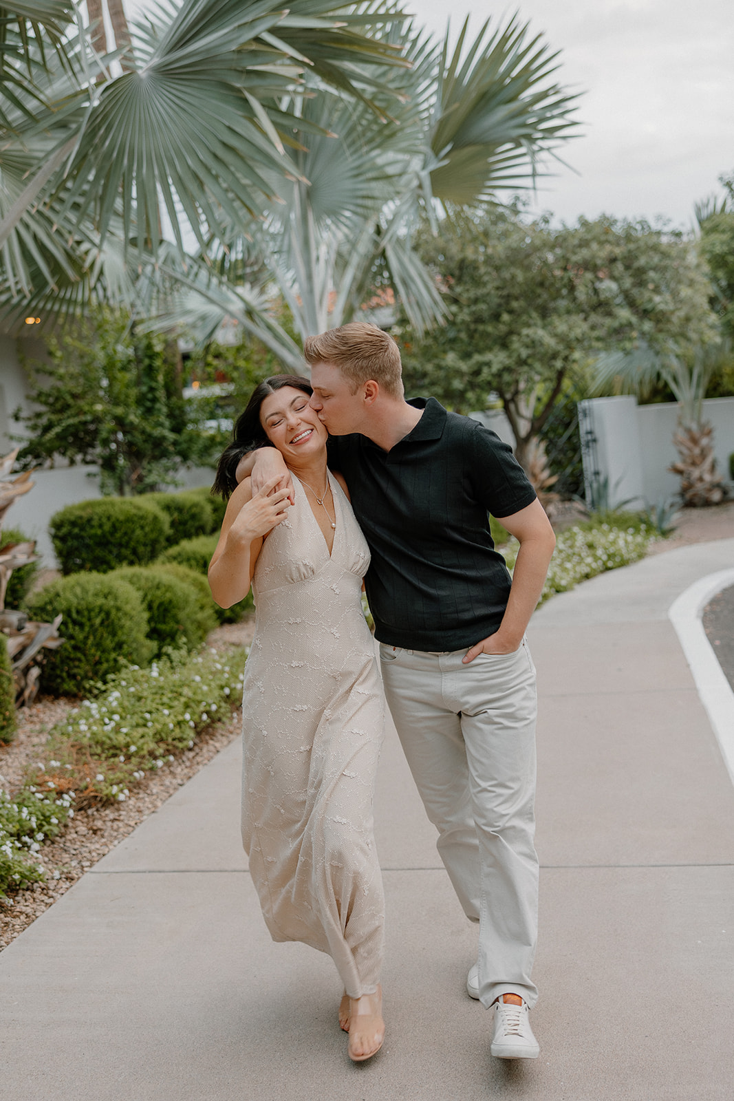 Couple walking together under palm trees during a relaxed resort engagement session
