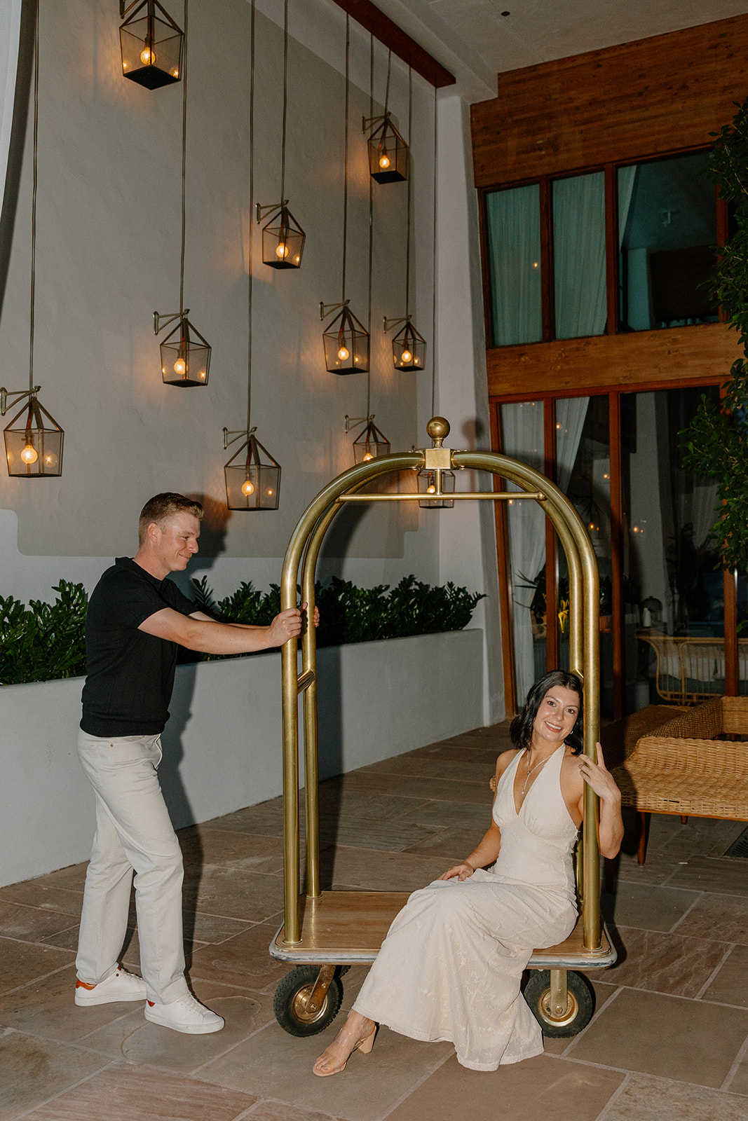 Hotel engagement photos of couple playing around with a luggage cart indoors
