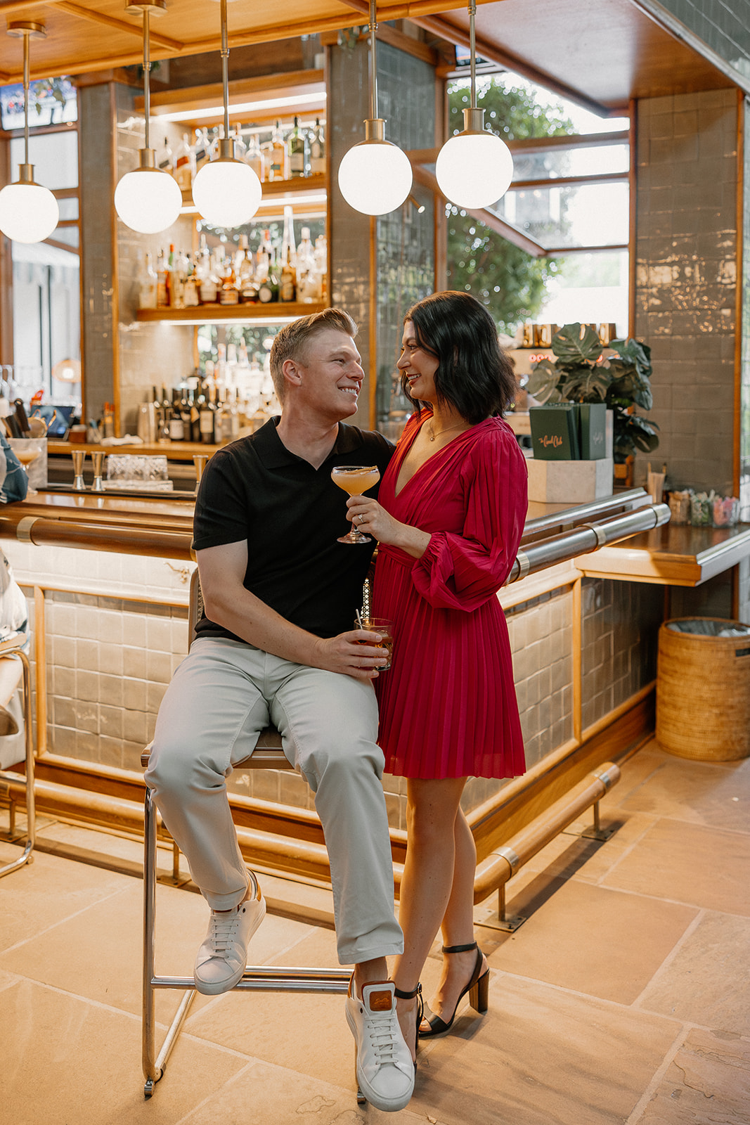 Hotel engagement photos at a bar with couple holding drinks and laughing together
