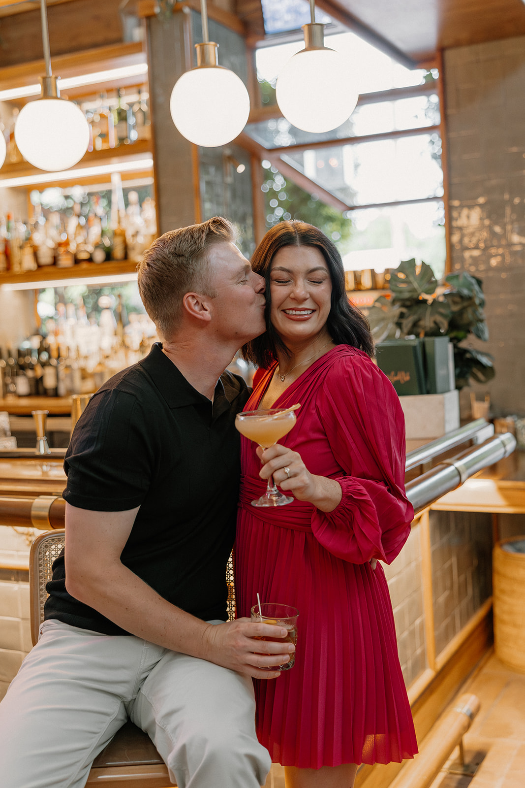 Hotel engagement photos at a bar with couple smiling and holding drinks
