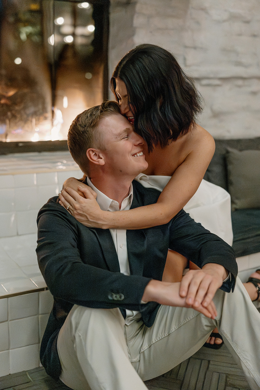 Couple cuddling by a fireplace during a cozy hotel engagement session

