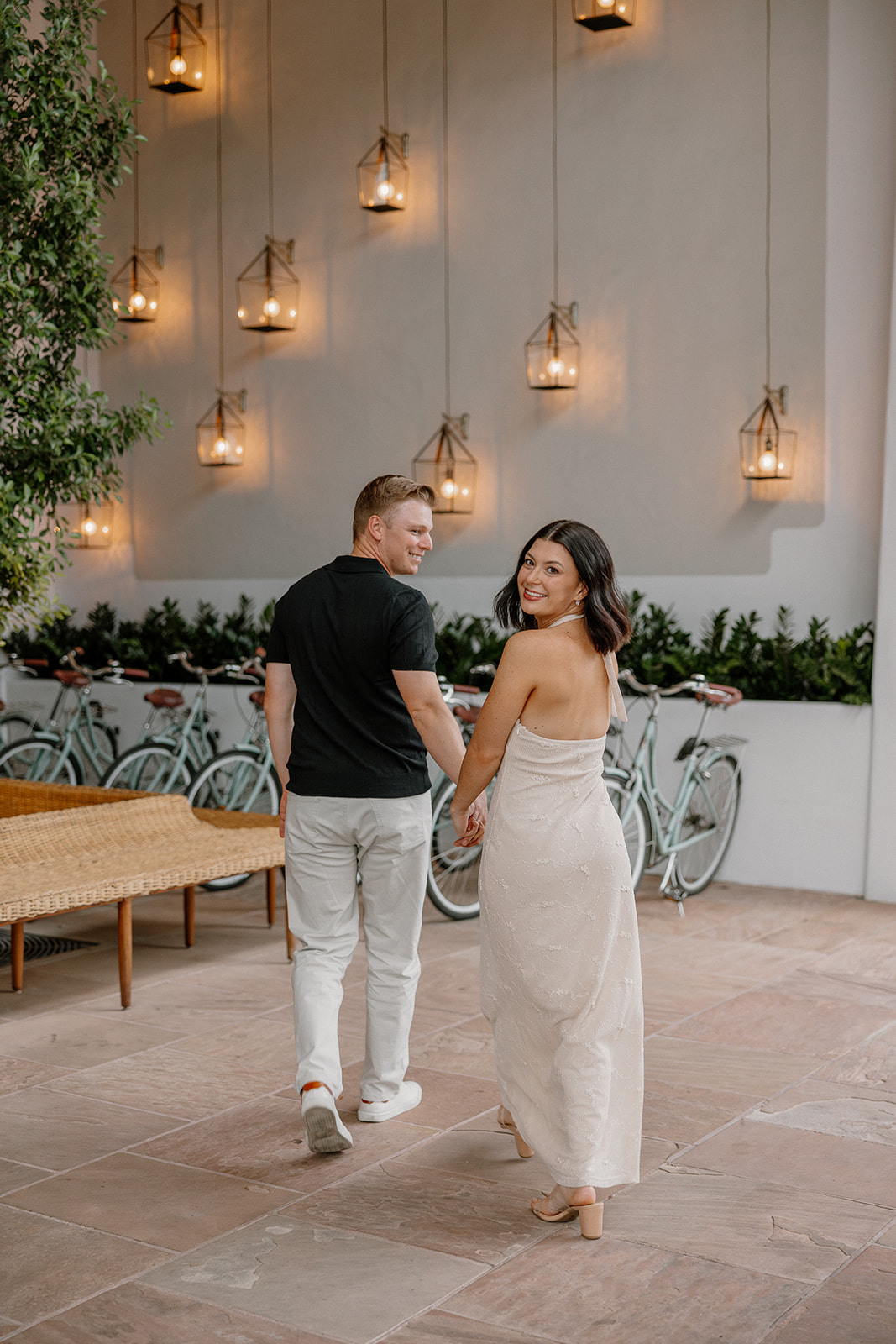 Couple walking away together in a courtyard with bikes and hanging lights at a resort
