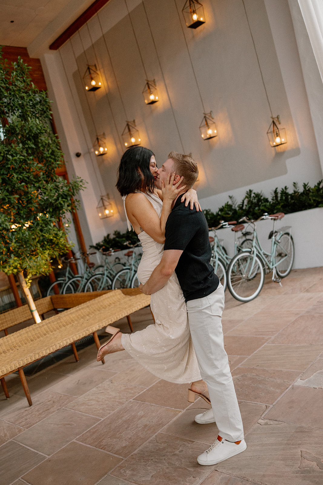 Couple kissing in a courtyard with hanging lanterns and bikes at a Scottsdale hotel
