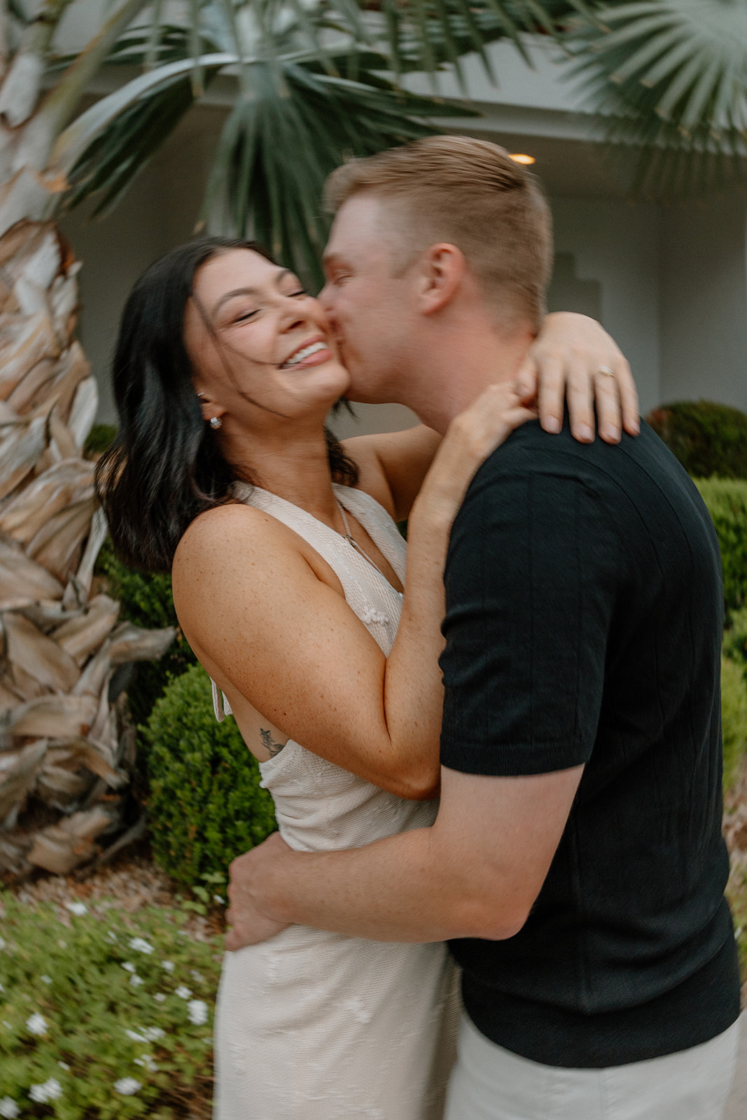 Romantic hotel engagement photos with couple hugging near palm trees outdoors
