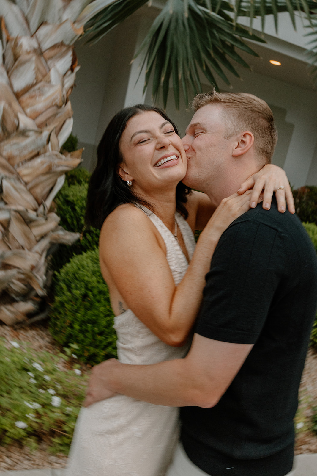 Couple laughing and hugging under palm trees during a relaxed resort engagement session