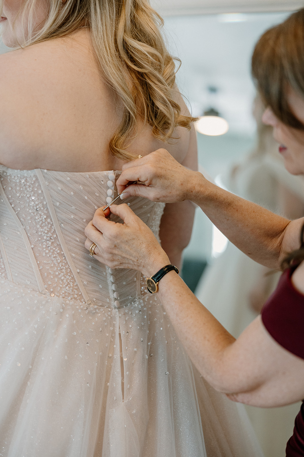 Mother helping bride button wedding dress during getting ready moments