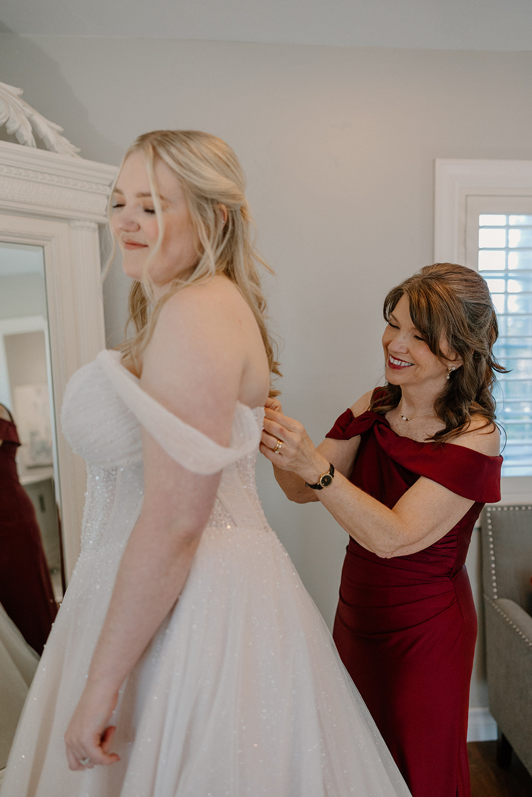 Mother helping bride into wedding dress in bridal suite at Stonebridge Manor Wedding Venue