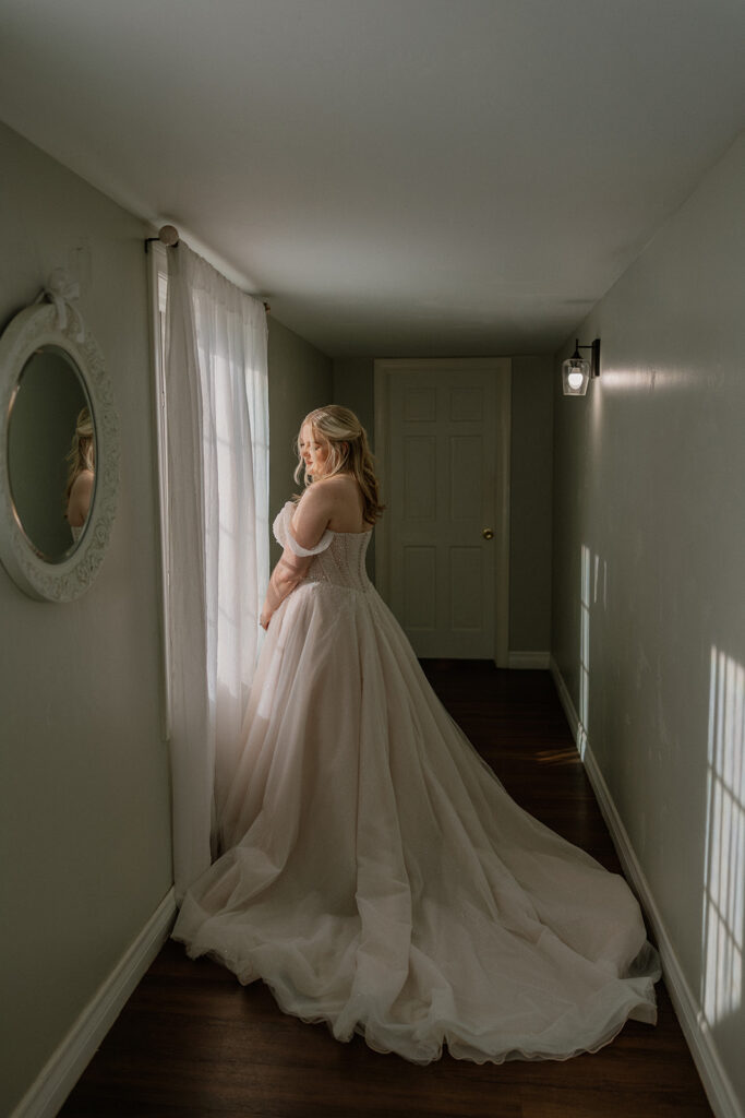 Bride standing by window in soft natural light at Stonebridge Manor Wedding Venue