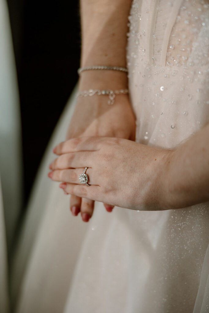 Close-up of bride’s engagement ring and bracelet against wedding dress fabric
