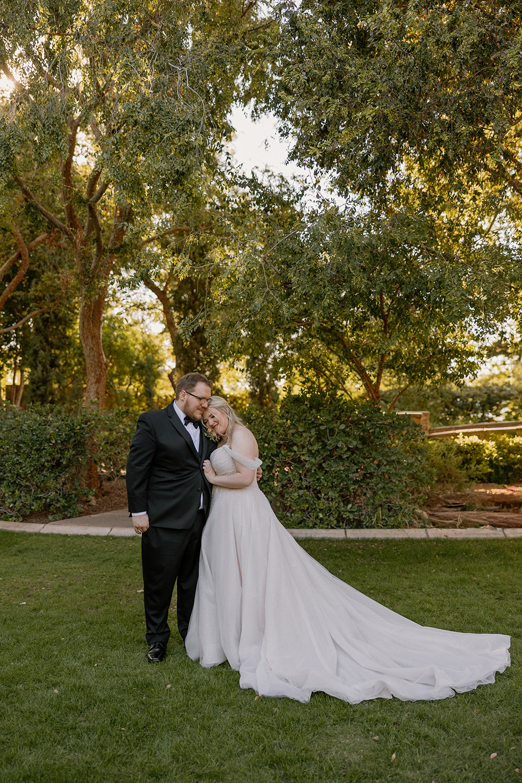 Newlywed couple embracing on the green lawn surrounded by trees at Stonebridge Manor Wedding Venue