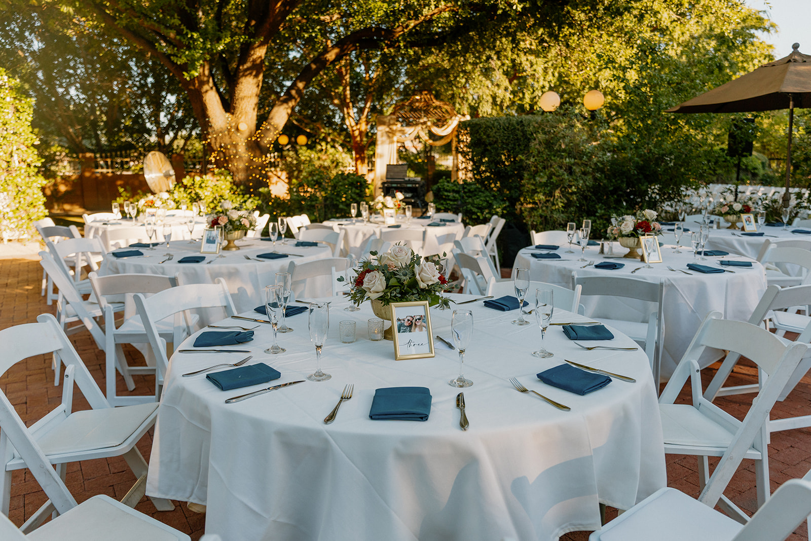 Wedding reception tables with blue napkins and floral centerpieces under trees