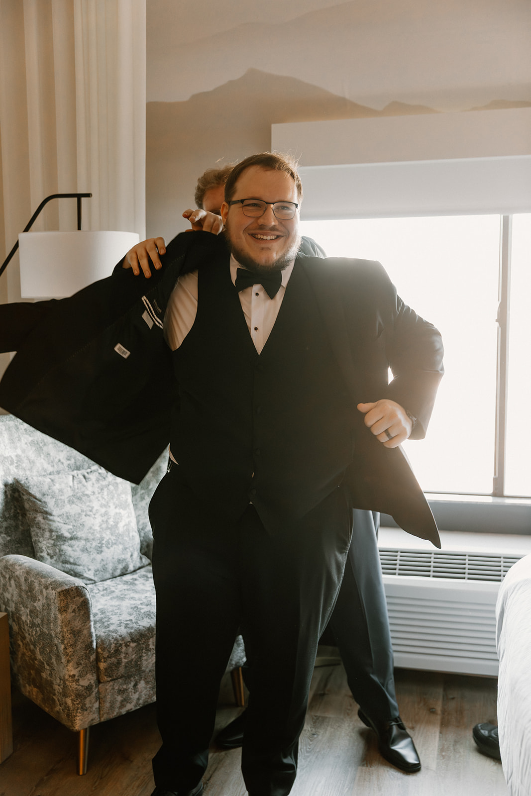 Groom putting on suit jacket with help from friend before wedding ceremony
