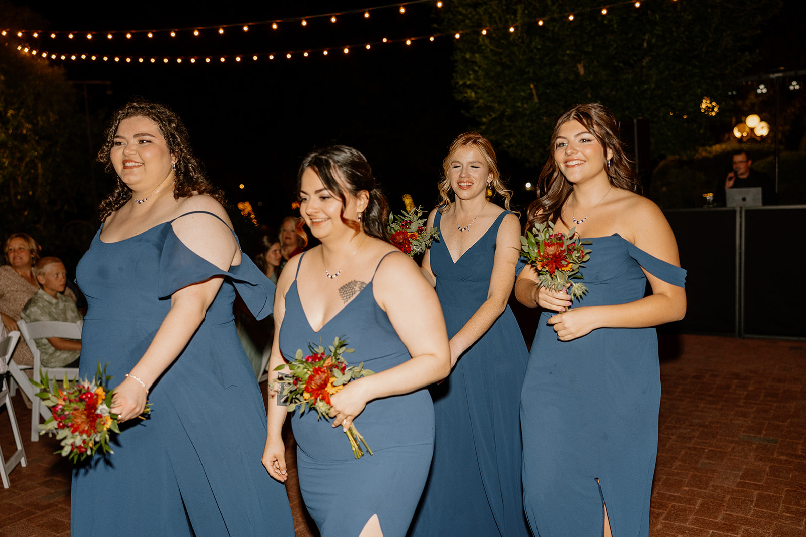 Bridesmaids walking into outdoor reception under string lights at Stonebridge Manor Wedding Venue
