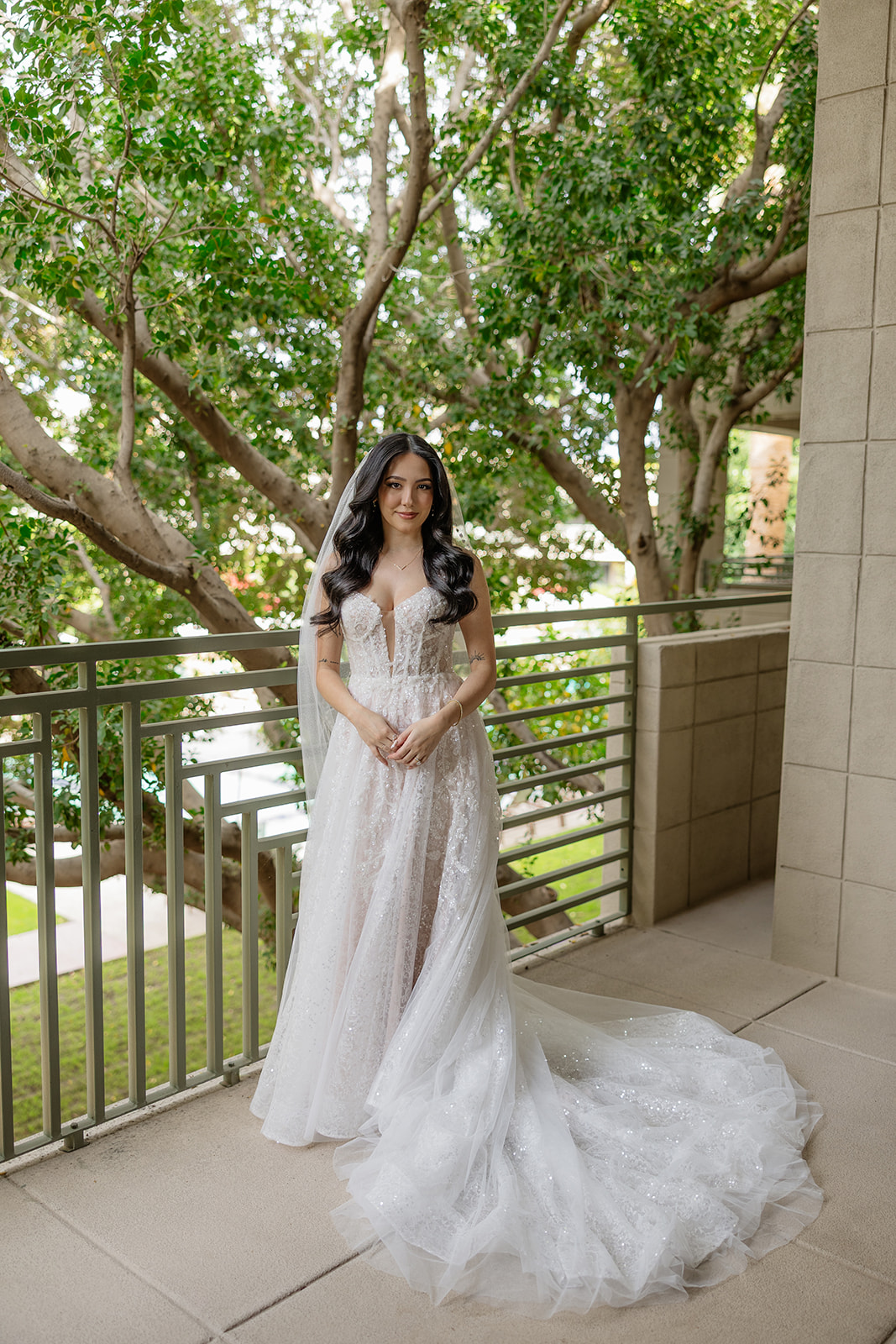 Bride standing on a balcony in her gown with trees in the background at the Biltmore wedding venue
