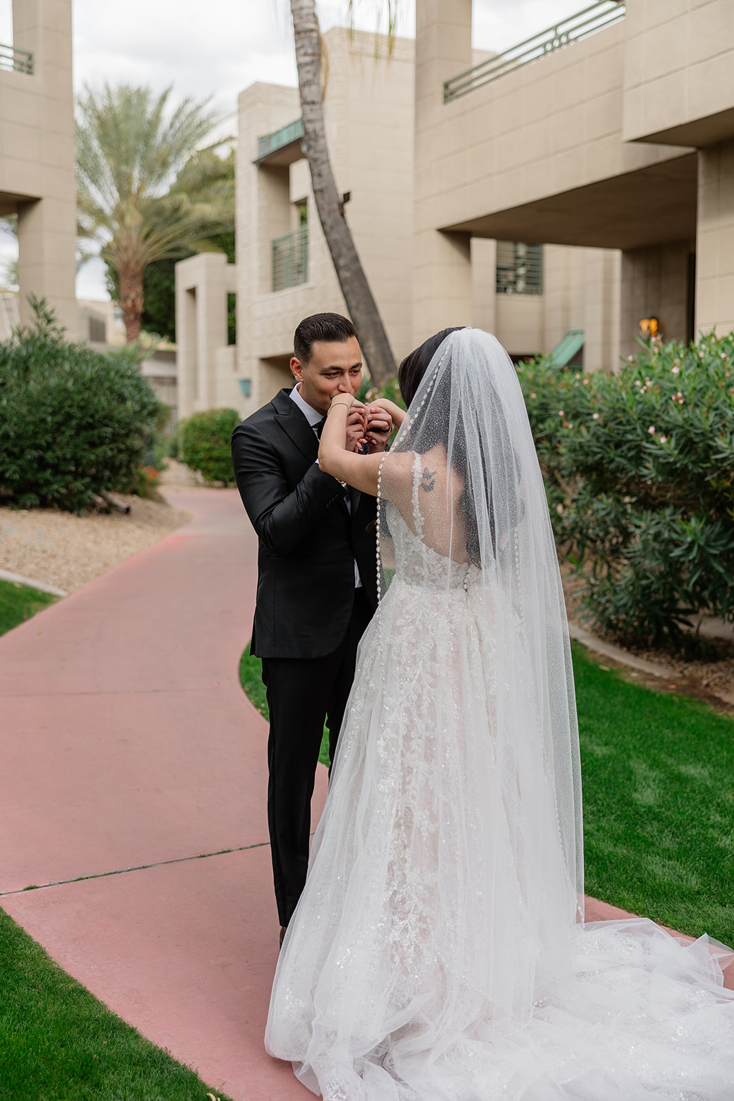 Groom kissing the bride’s hands as they stand together on a garden path
